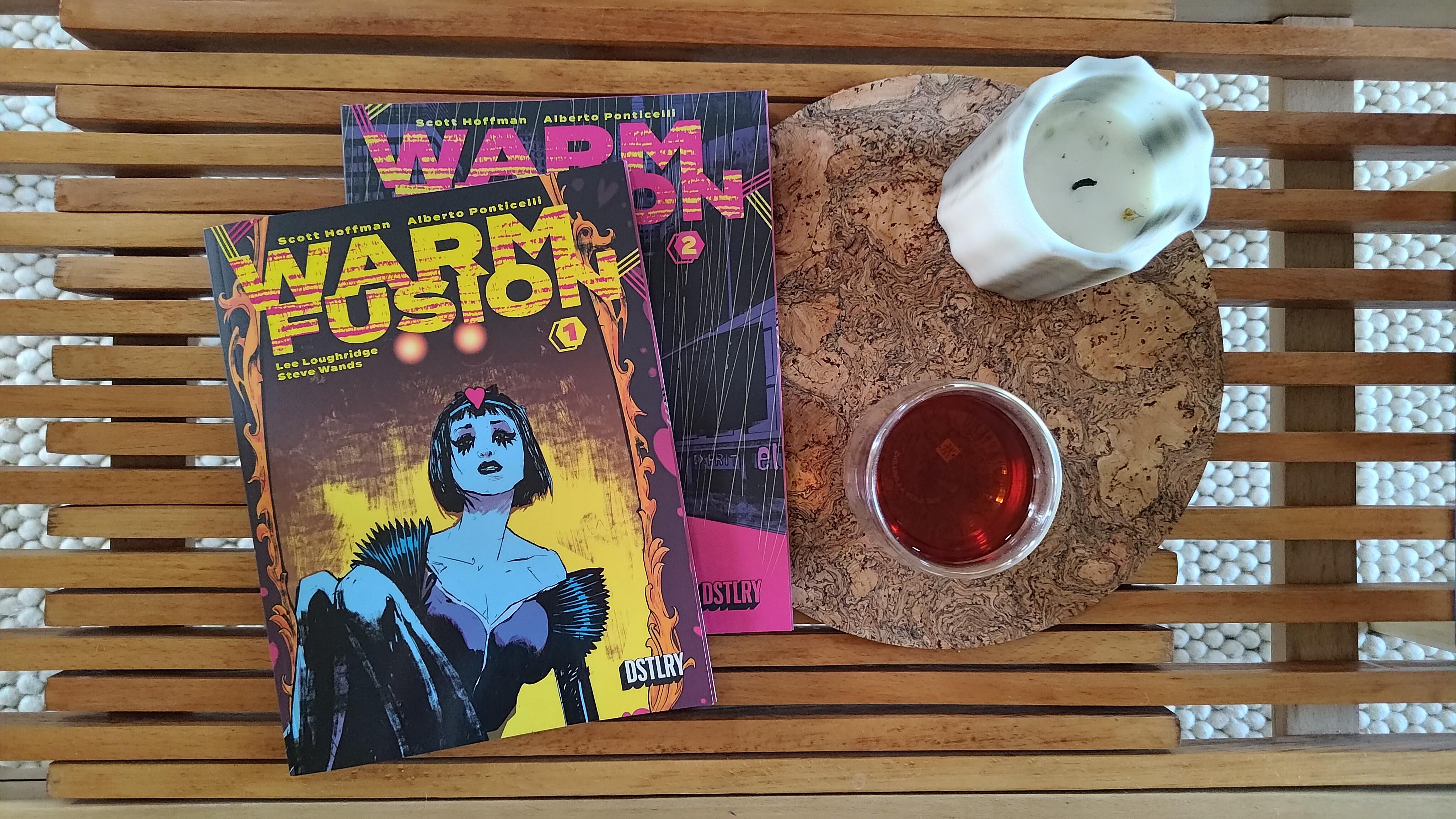 Issues 1 and 2 of Warm Fusion laid out on a midcentury coffee table with a glass of tea